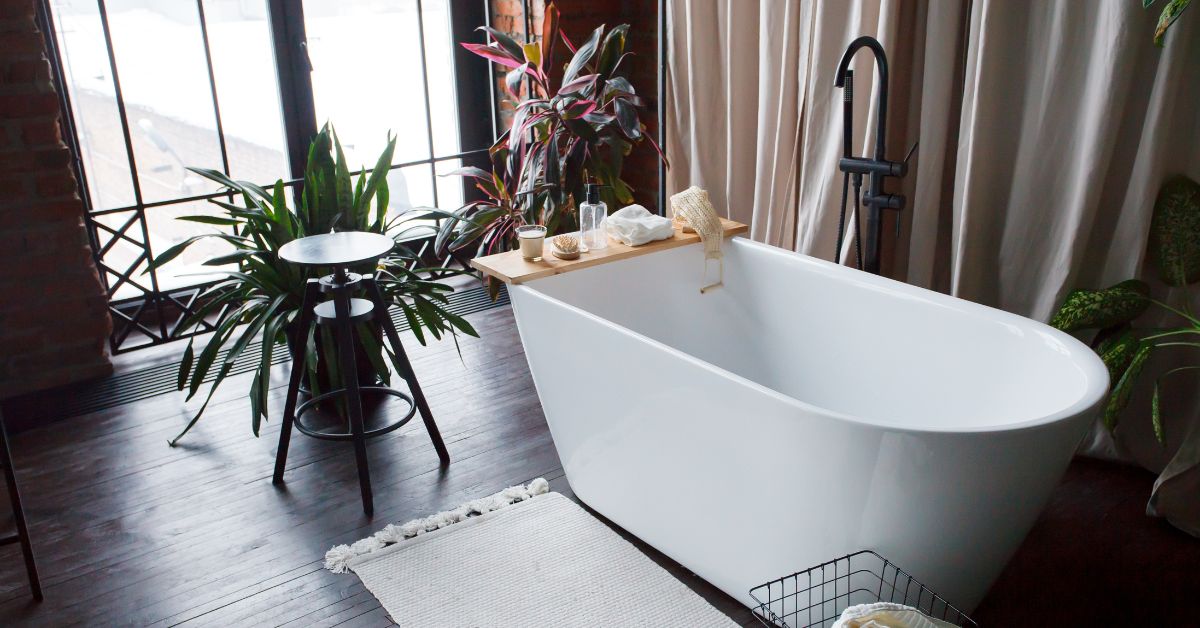 Modern bathroom with freestanding white acrylic bathtub and black loft mixer. Walls made of bricks, big window, parquet is wooden on floor