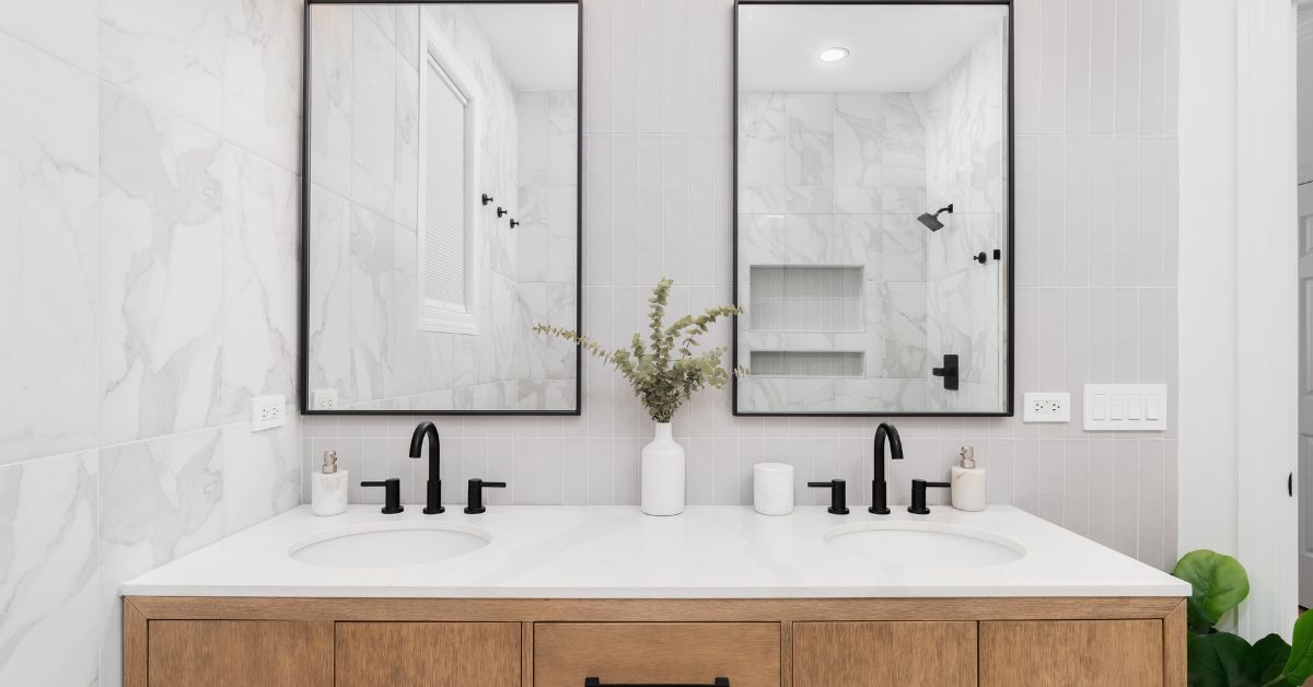 A bathroom with marble and stacked vertical subway tiles, a white oak vanity cabinet, black framed square mirrors and faucets, and marble countertop.